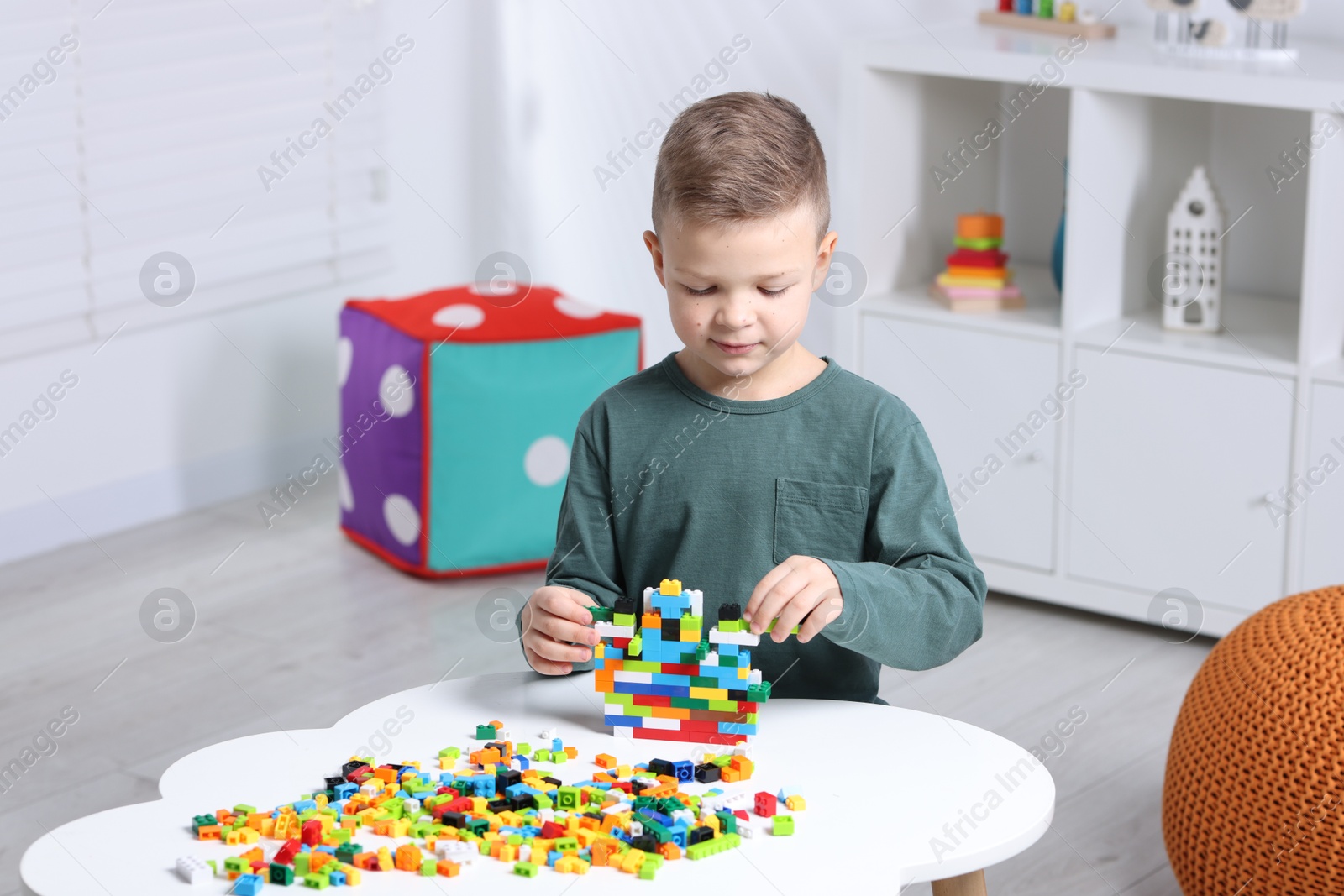 Photo of Cute boy playing with building blocks at white table indoors. Space for text