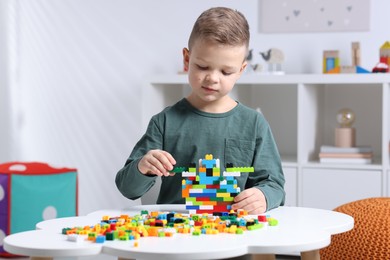 Photo of Cute boy playing with building blocks at white table indoors