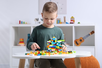 Photo of Cute boy playing with building blocks at white table indoors