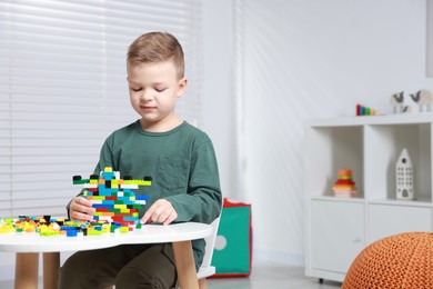 Photo of Cute boy playing with building blocks at white table indoors. Space for text