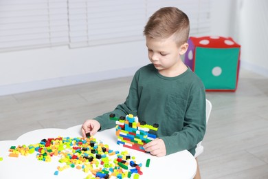 Cute boy playing with building blocks at white table indoors. Space for text