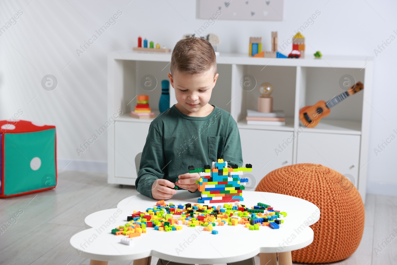 Photo of Cute boy playing with building blocks at white table indoors