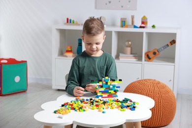 Cute boy playing with building blocks at white table indoors