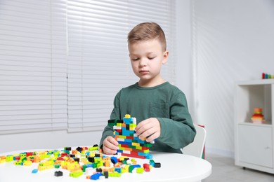 Photo of Cute boy playing with building blocks at white table indoors