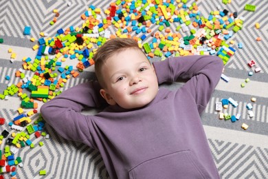 Photo of Cute boy and colorful building blocks on floor, top view