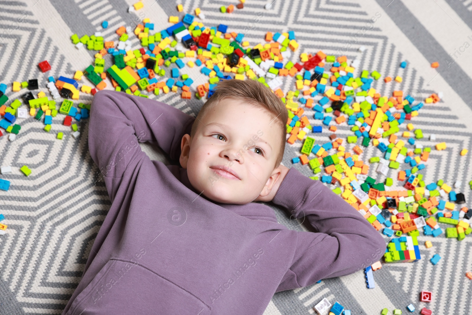 Photo of Cute boy and colorful building blocks on floor, top view