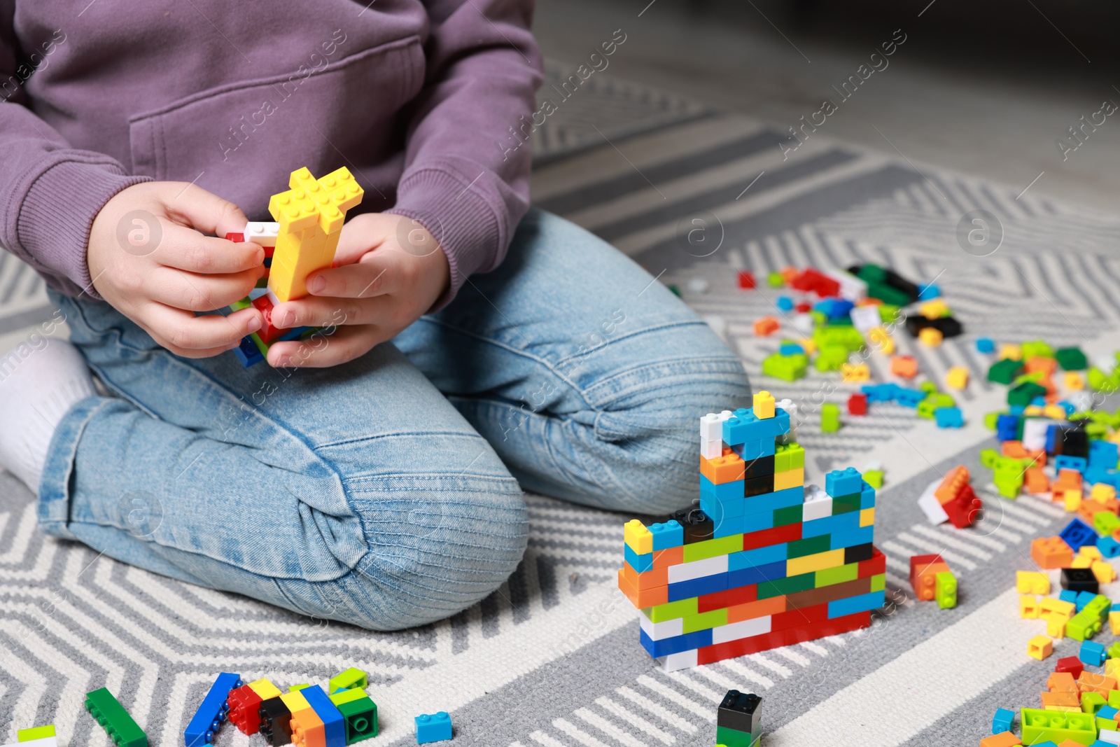 Photo of Cute boy playing with building blocks on floor at home, closeup