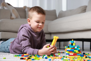 Photo of Cute boy playing with building blocks on floor at home. Space for text