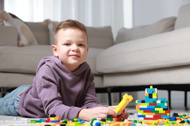 Photo of Cute boy playing with building blocks on floor at home. Space for text