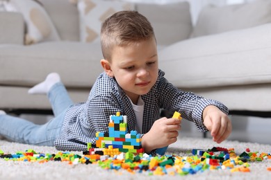 Cute boy playing with building blocks on floor at home