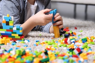 Photo of Cute boy playing with building blocks on floor at home, closeup