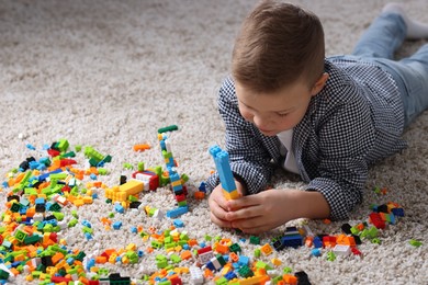 Cute boy playing with building blocks on floor at home