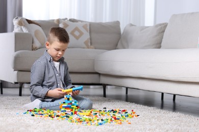 Photo of Cute boy playing with building blocks on floor at home. Space for text