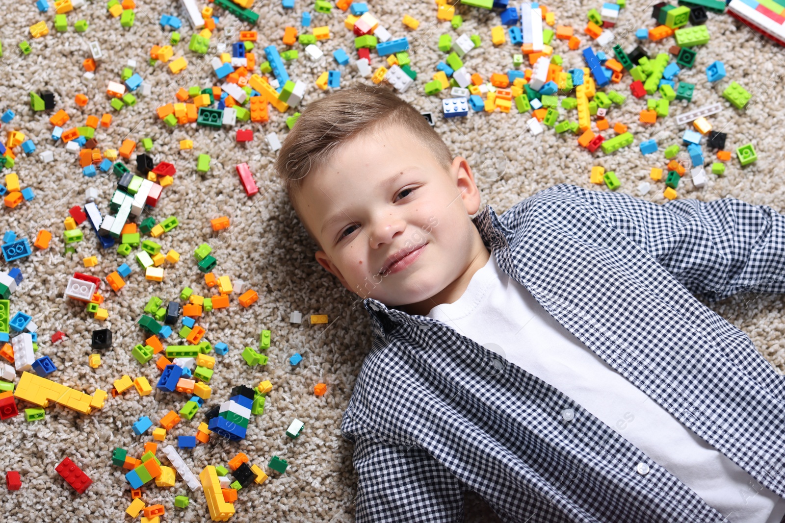 Photo of Cute boy and colorful building blocks on floor, top view