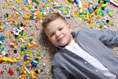 Cute boy and colorful building blocks on floor, top view