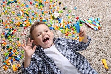 Photo of Cute boy and colorful building blocks on floor, top view