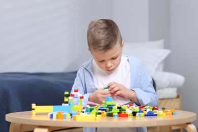 Photo of Cute boy playing with building blocks at wooden table indoors