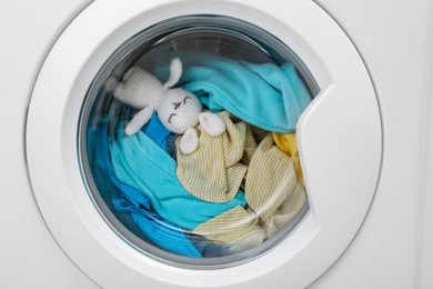 Photo of Washing machine with clothes and toy bunny as background, closeup