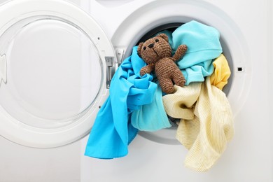 Photo of Washing machine with clothes and toy bear near light wall, closeup