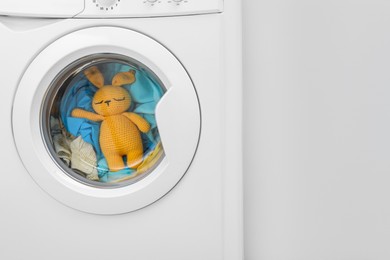 Photo of Washing machine with clothes and toy bunny near light wall, closeup. Space for text