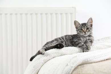 Photo of Cute little kitten on pouf near radiator at home