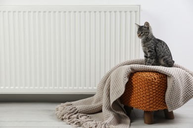 Photo of Cute little kitten on pouf near radiator at home, space for text