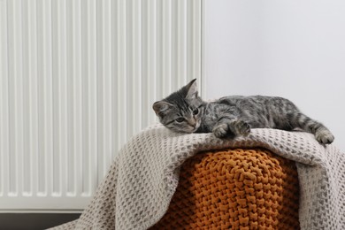 Photo of Cute little kitten on pouf near radiator at home