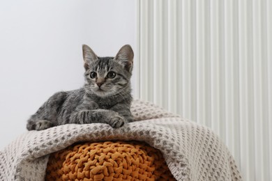 Photo of Cute little kitten on pouf near radiator at home