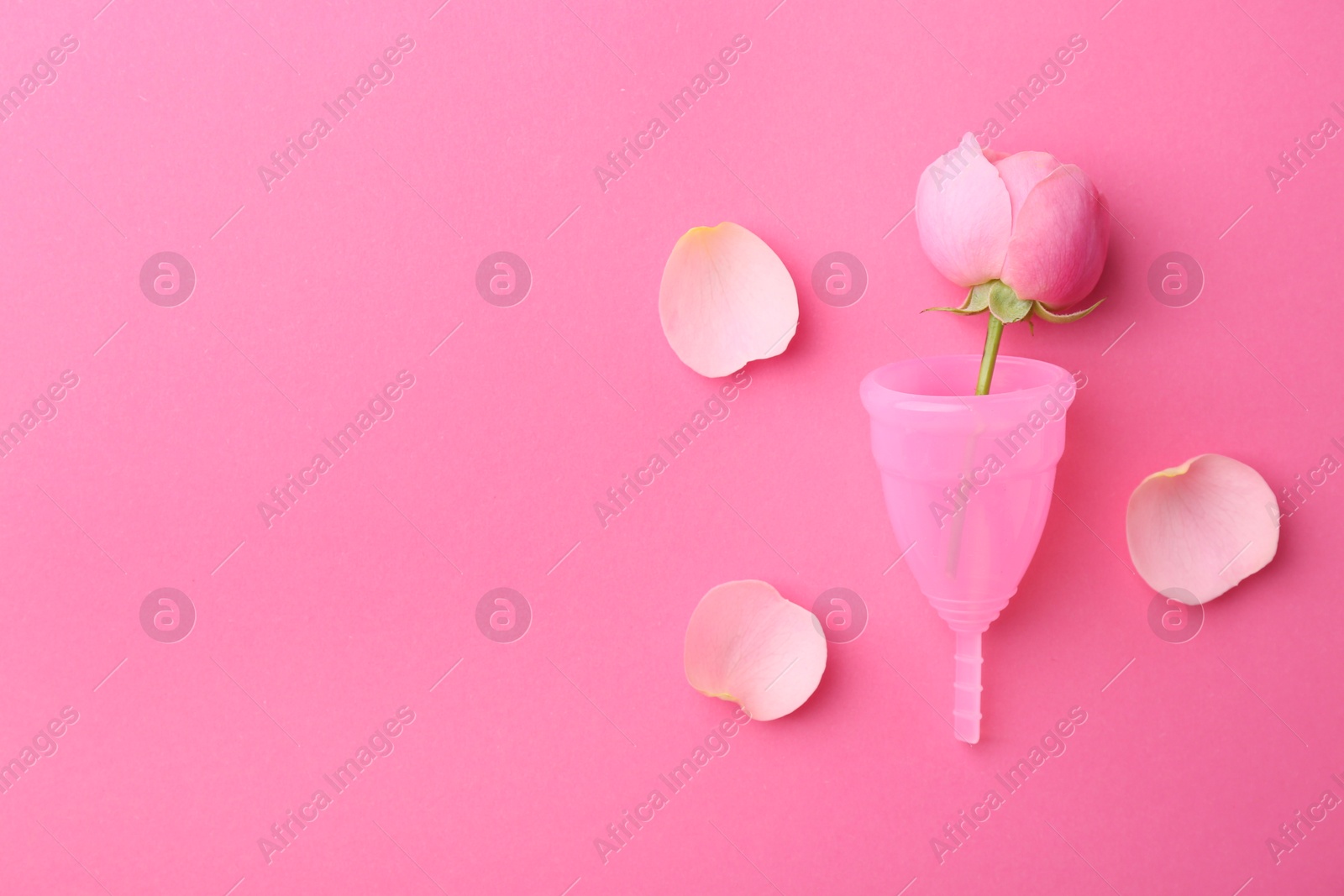 Photo of Menstrual cup and flower on pink background, top view. Space for text