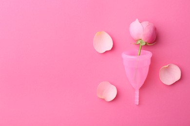 Photo of Menstrual cup and flower on pink background, top view. Space for text