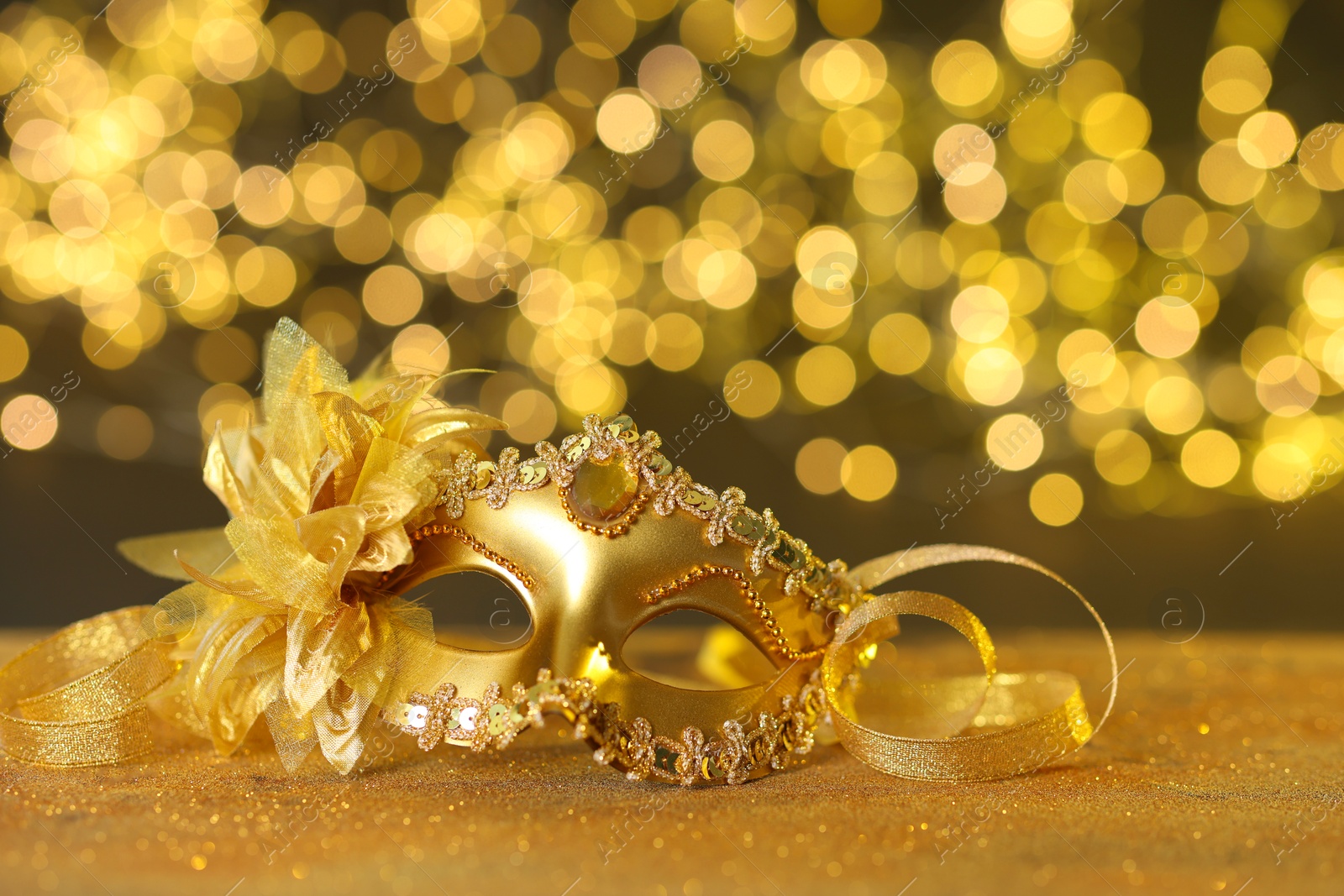 Photo of Beautiful carnival mask on golden shiny surface against blurred lights