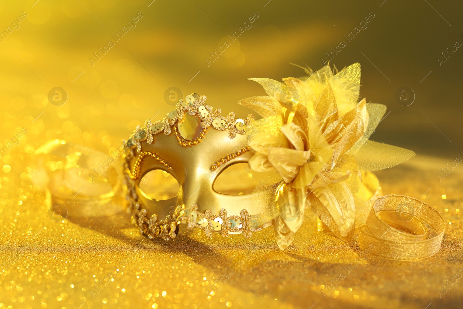 Photo of Beautiful carnival mask on golden shiny surface, closeup