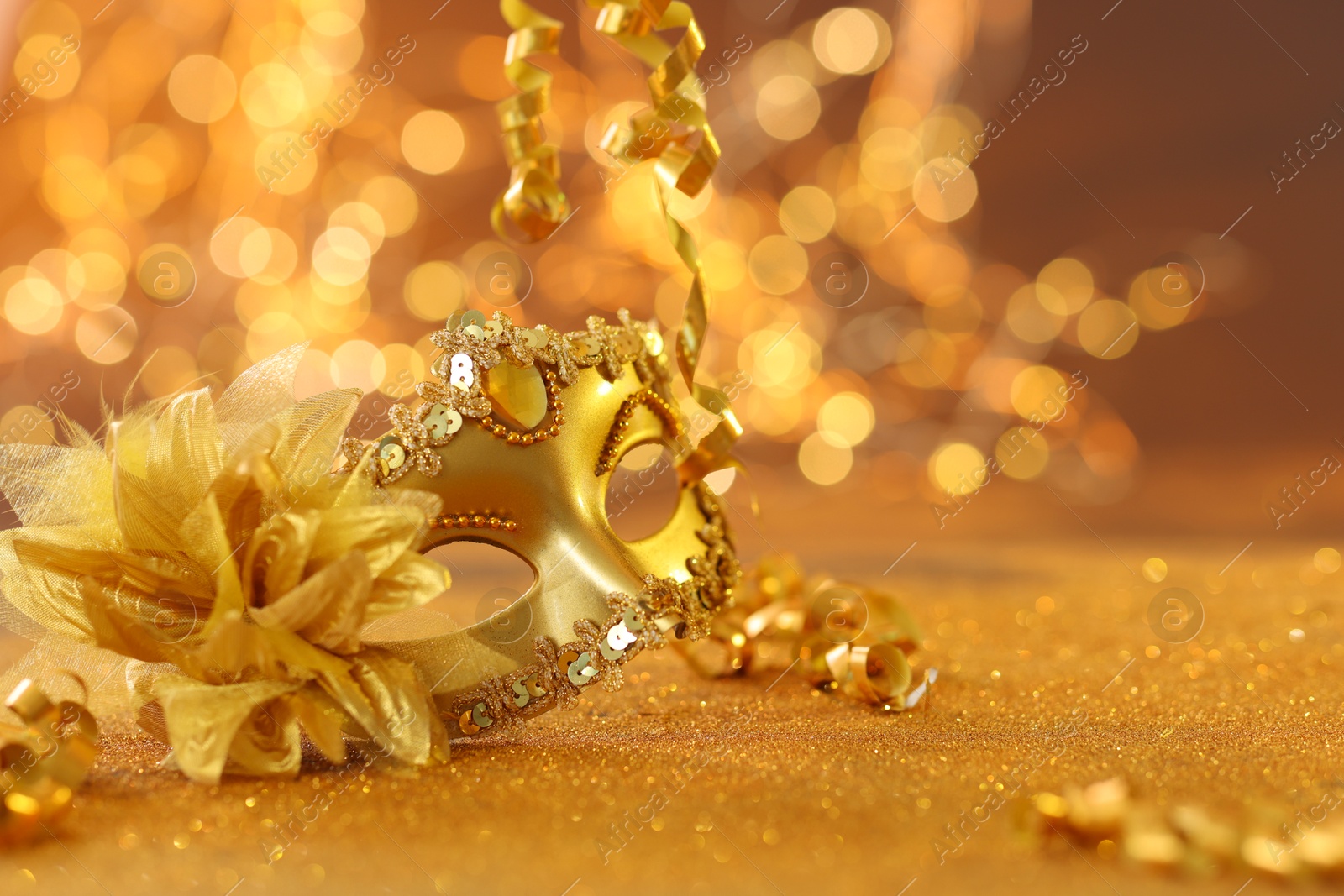 Photo of Beautiful carnival mask on golden shiny surface, closeup. Space for text