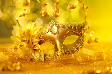 Photo of Beautiful carnival mask on golden shiny surface, closeup