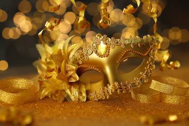 Photo of Beautiful carnival mask on golden shiny surface against blurred lights, closeup