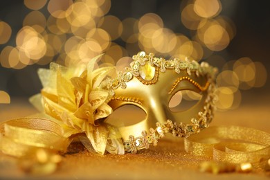 Photo of Beautiful carnival mask on golden shiny surface against blurred lights, closeup