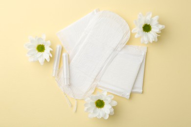 Photo of Menstrual pads, flowers and tampons on beige background, flat lay