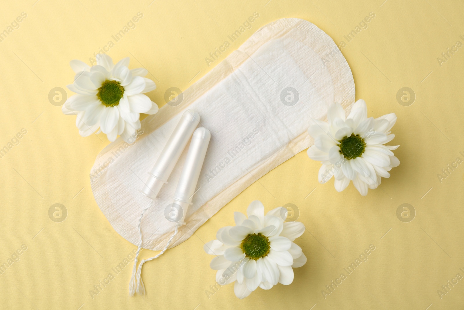 Photo of Menstrual pad, flowers and tampons on beige background, flat lay