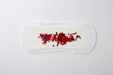 Photo of Menstrual pad with red sequins on white background, top view