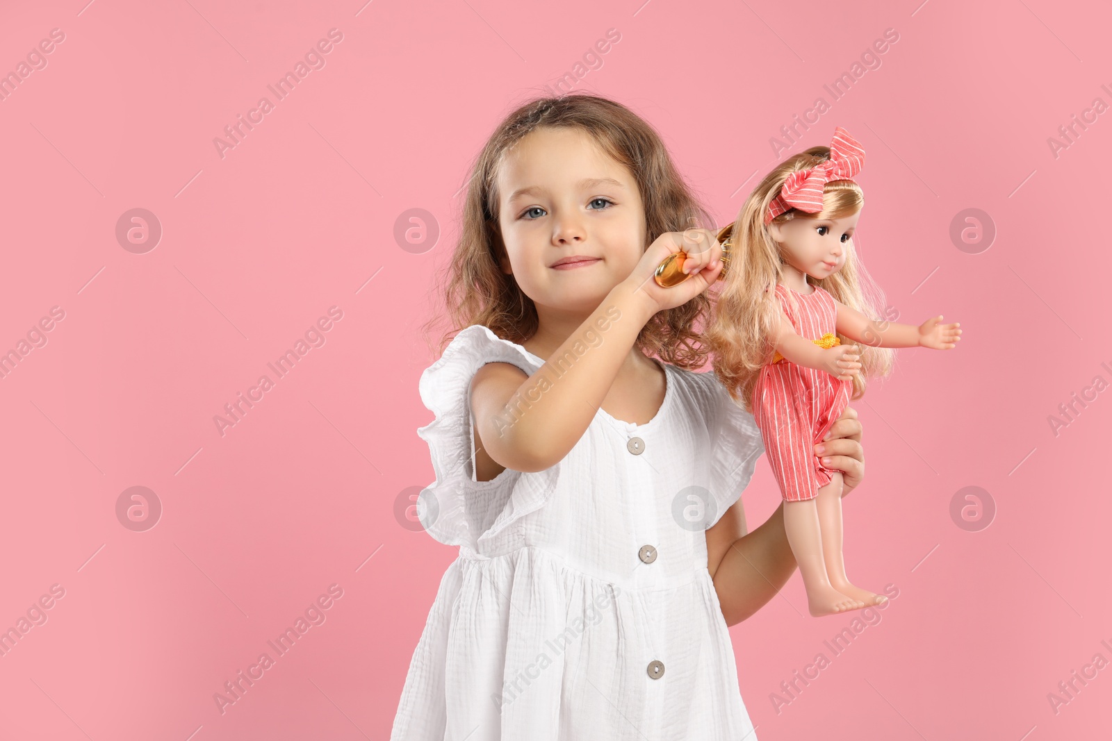 Photo of Cute little girl brushing doll's hair on pink background