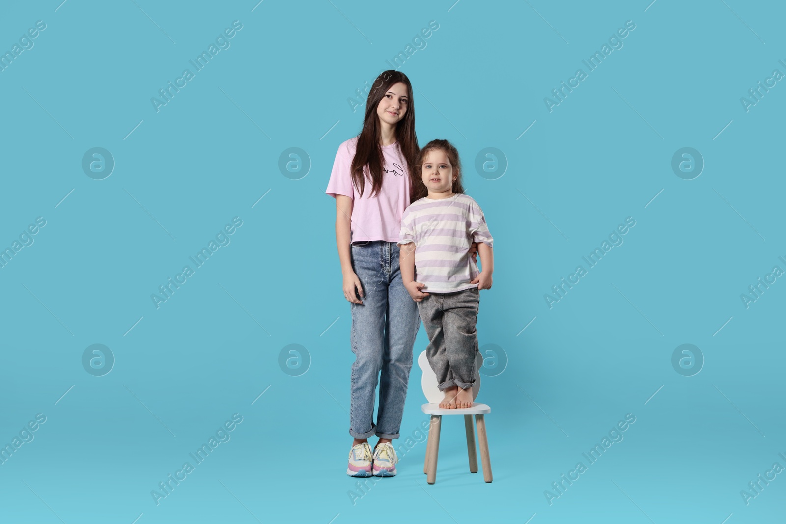 Photo of Portrait of cute sisters on light blue background