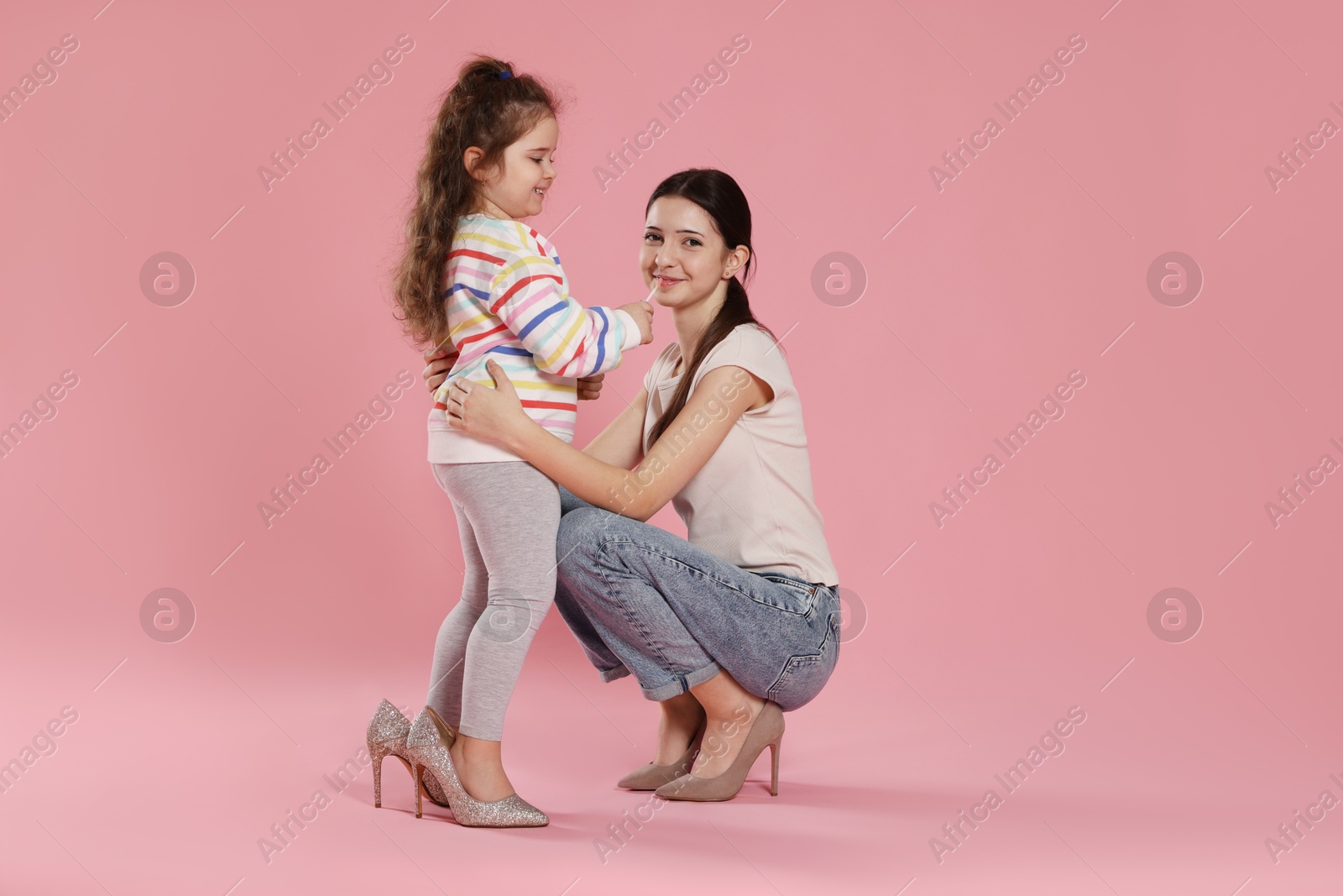 Photo of Cute little girl with lip gloss and her sister on pink background