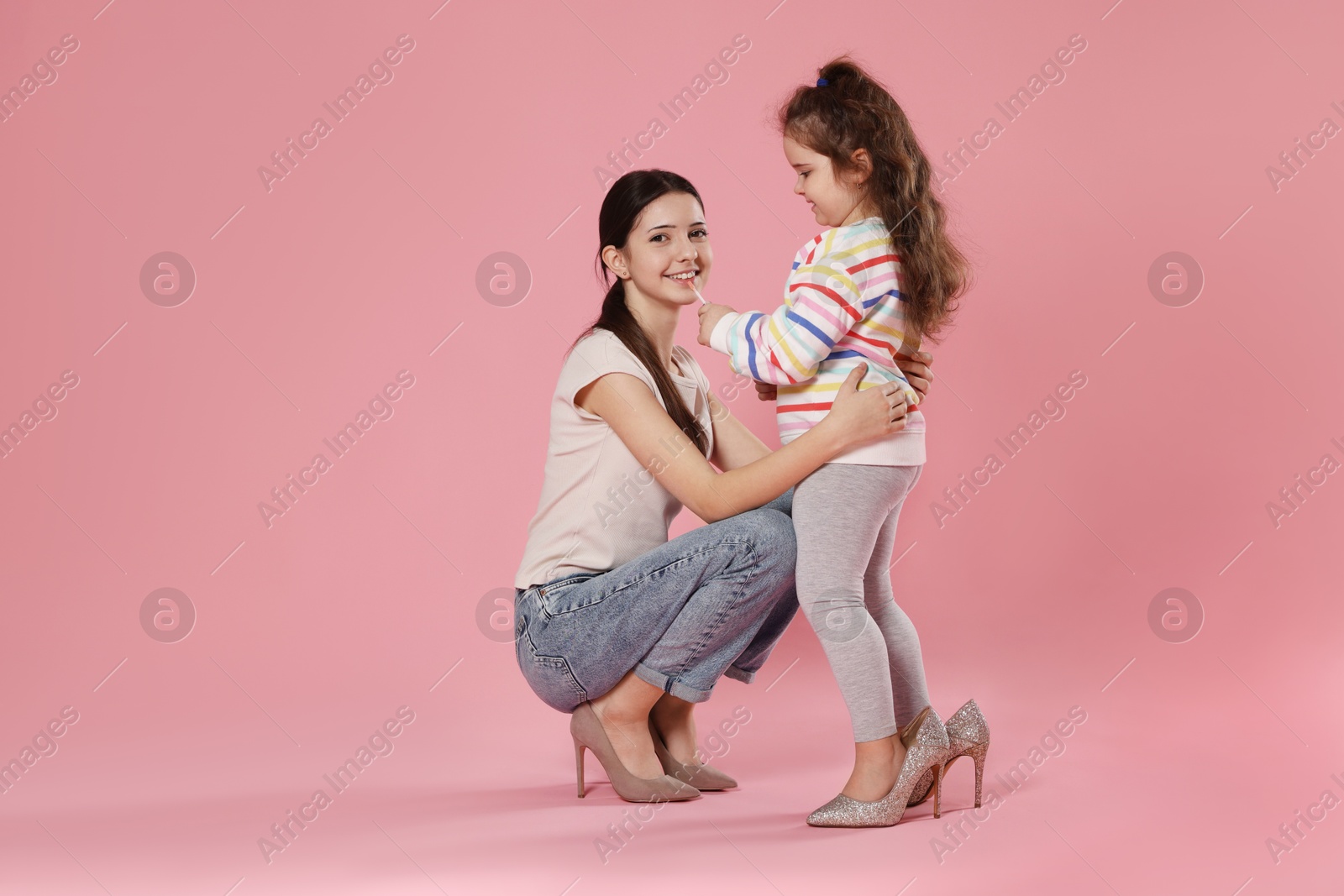 Photo of Cute little girl with lip gloss and her sister on pink background