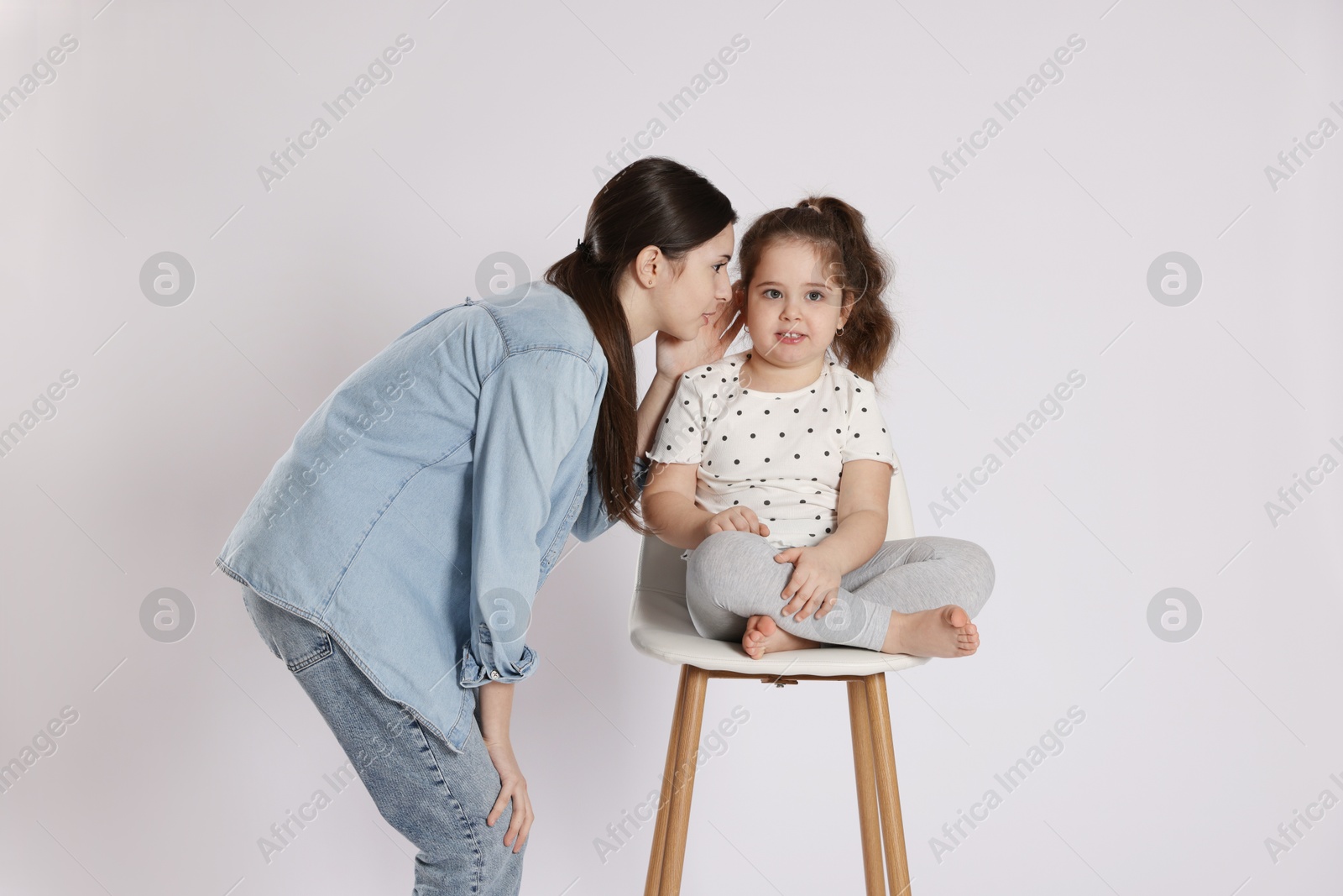 Photo of Teenage girl whispering secret to her cute little sister on white background