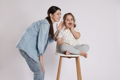 Photo of Teenage girl whispering secret to her cute little sister on white background