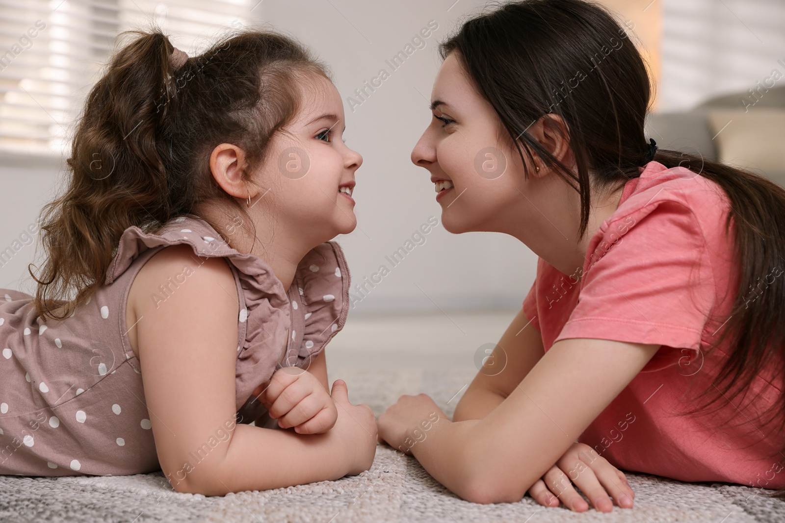 Photo of Cute little girl and her sister on rug at home