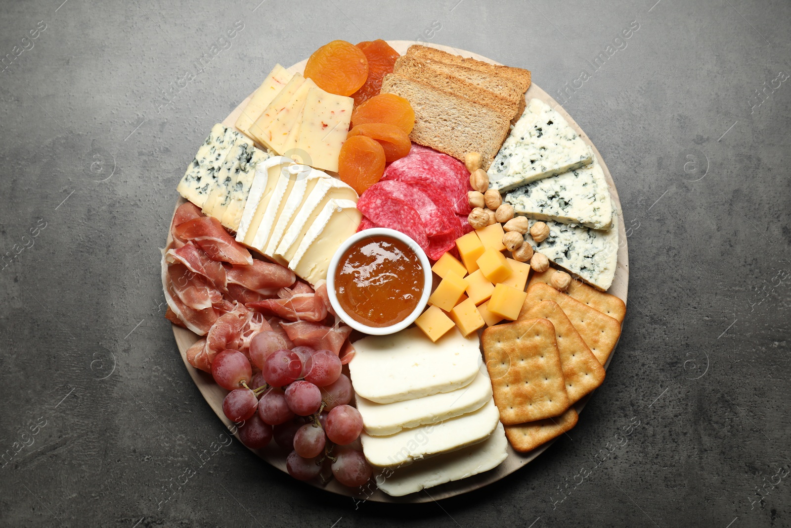 Photo of Different types of cut cheese and other snacks on grey textured table, top view