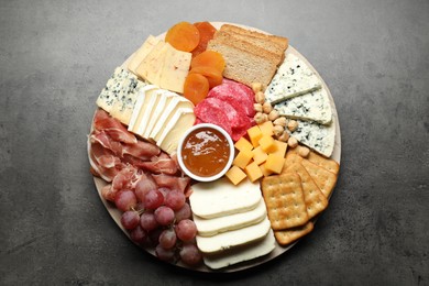 Photo of Different types of cut cheese and other snacks on grey textured table, top view