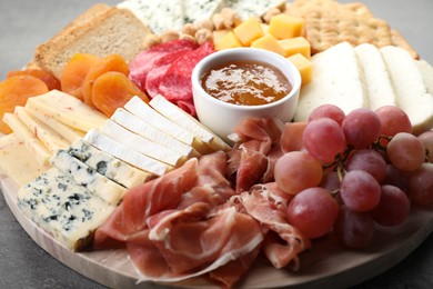 Photo of Different types of cut cheese and other snacks on grey textured table, closeup