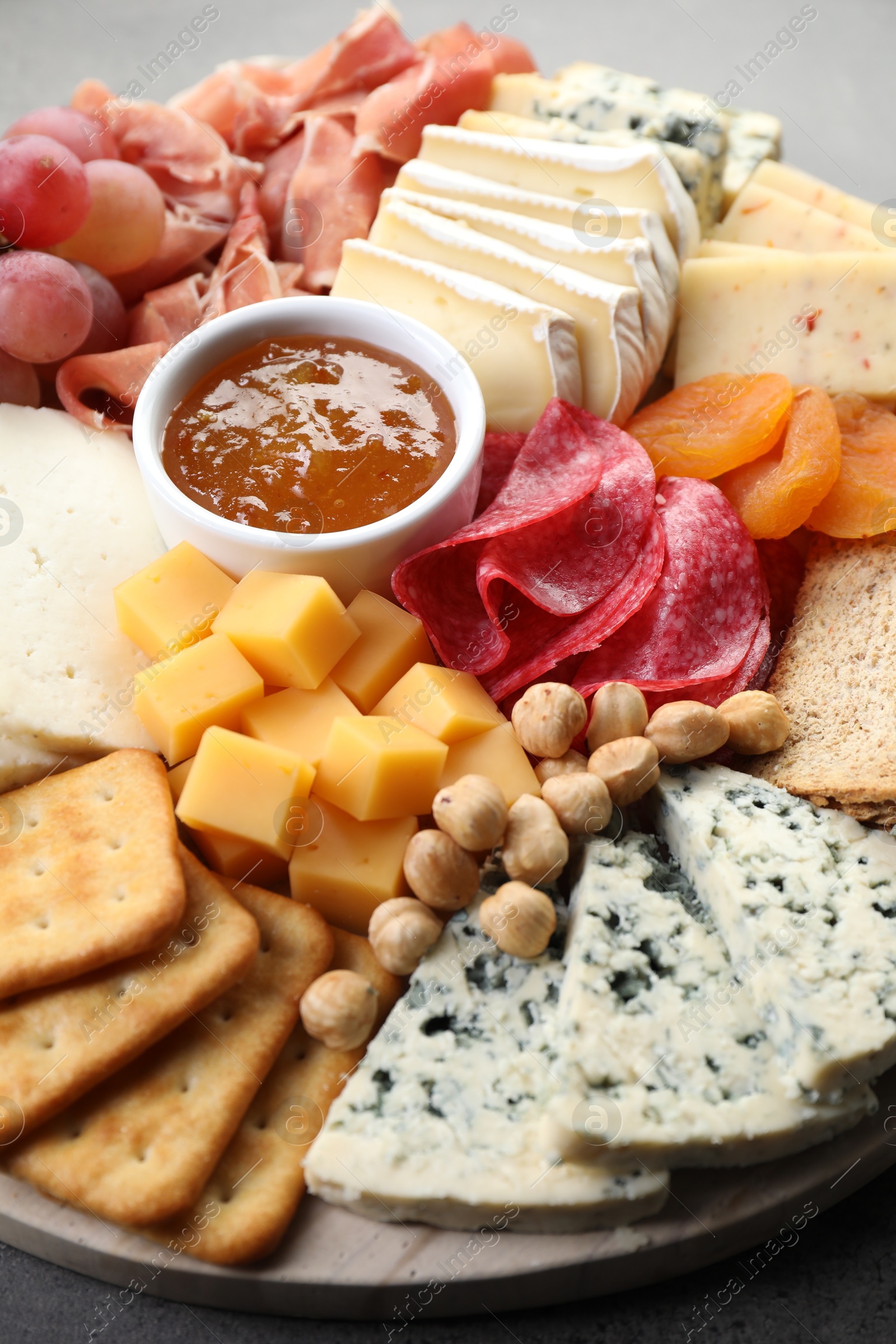 Photo of Different types of cut cheese and other snacks on grey textured table, closeup